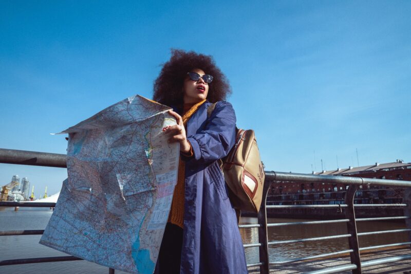 Black woman holding out a map while looking around.