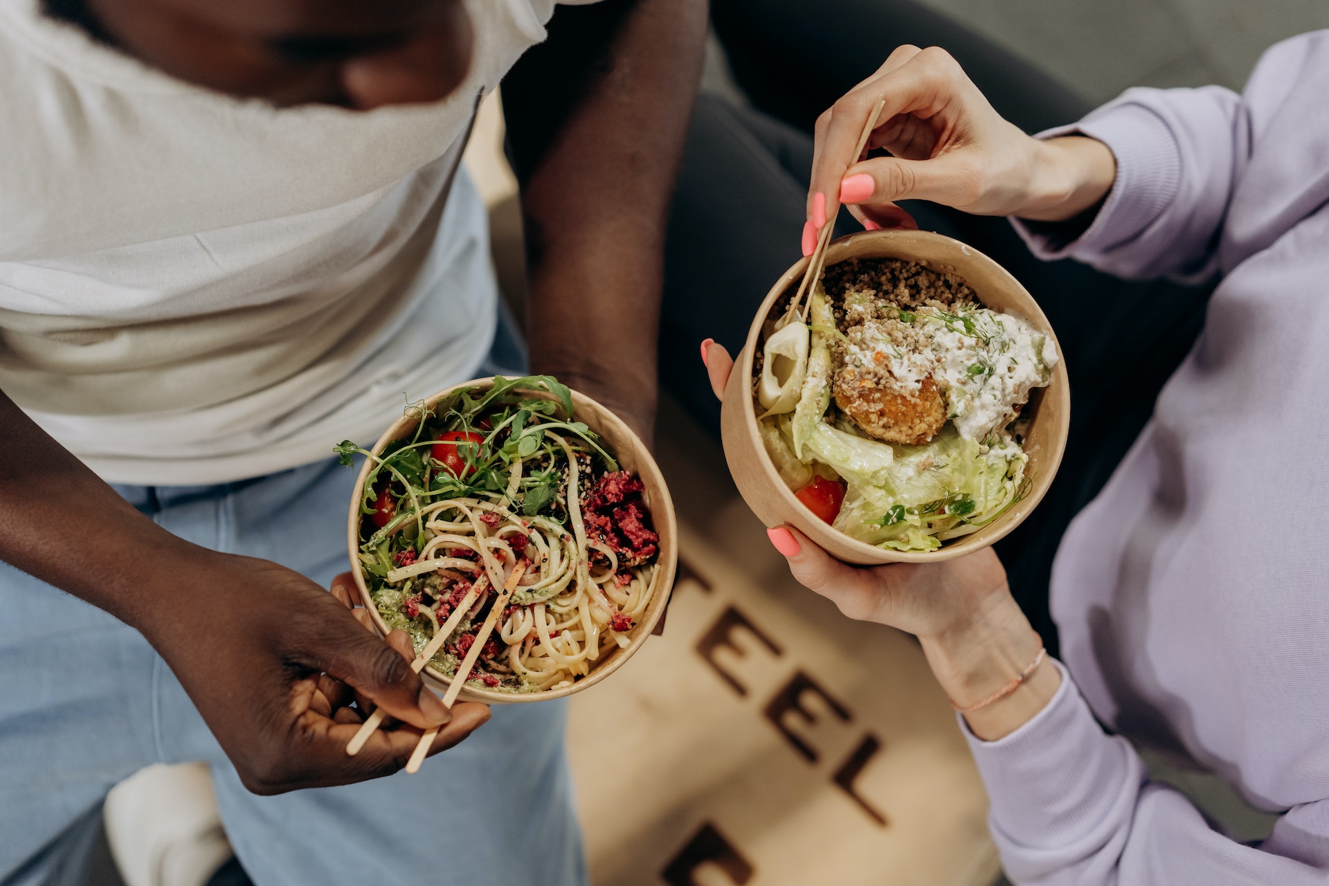 Two people eating out of takeout bowls with chopsticks
