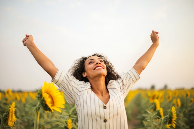 Woman standing in a field of sunflowers raising her hands in the air and smiling