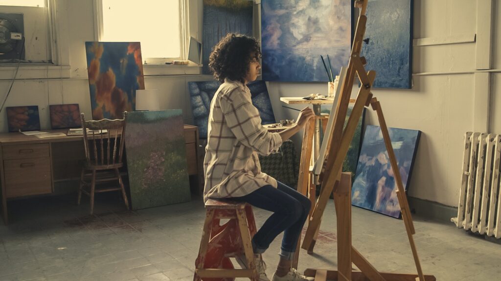 A female black artist sitting at an easel and painting