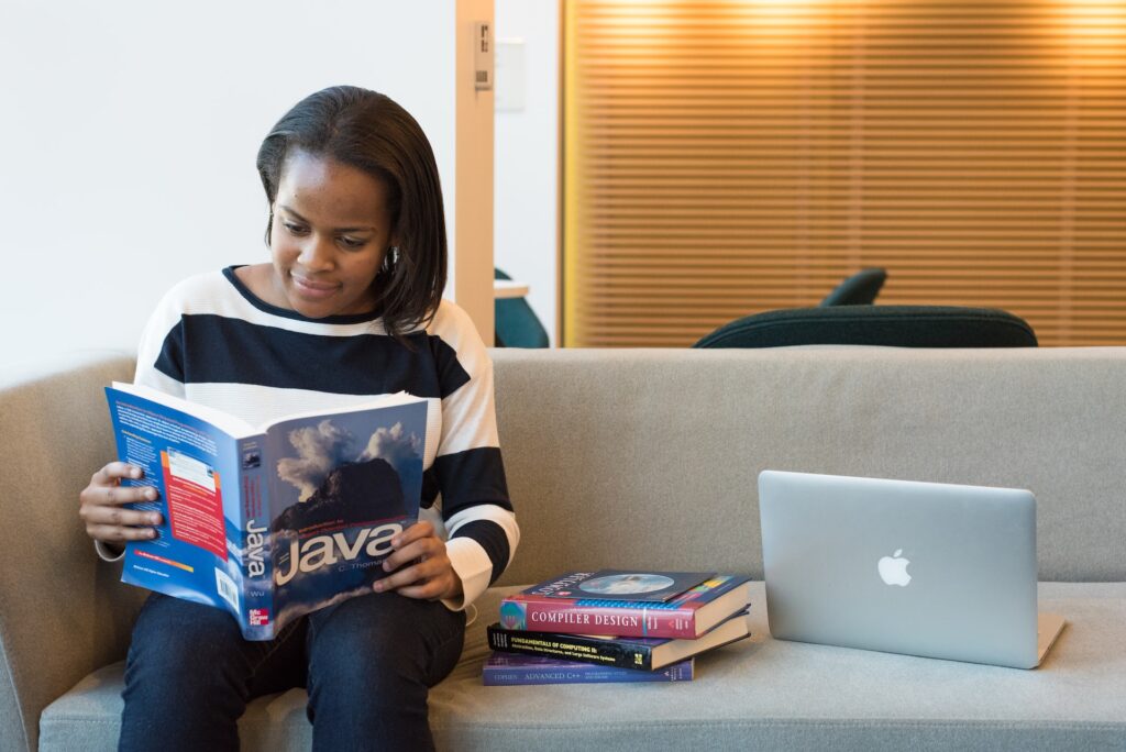 A black woman sitting on a couch reading a book about coding