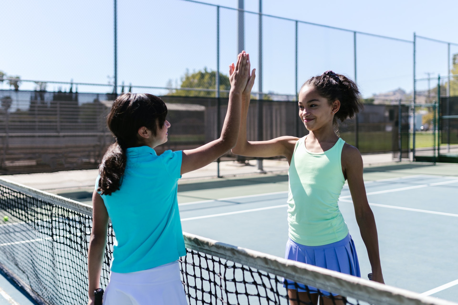 Two young girls giving each other a high-five across a tennis net