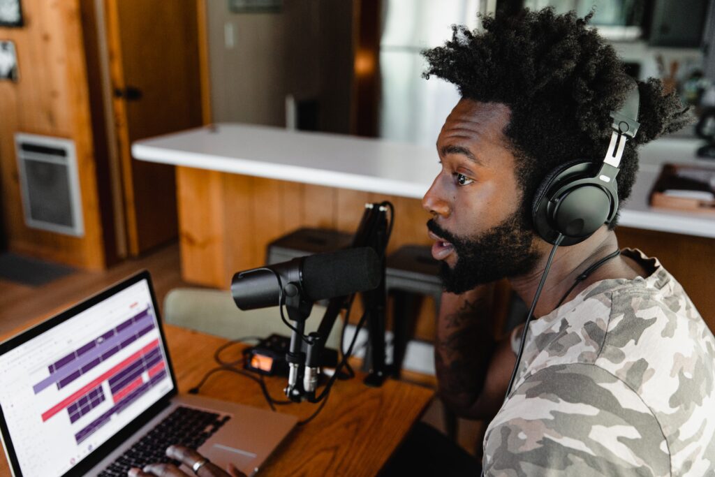 A black man sitting in front of a computer and talking into a microphone