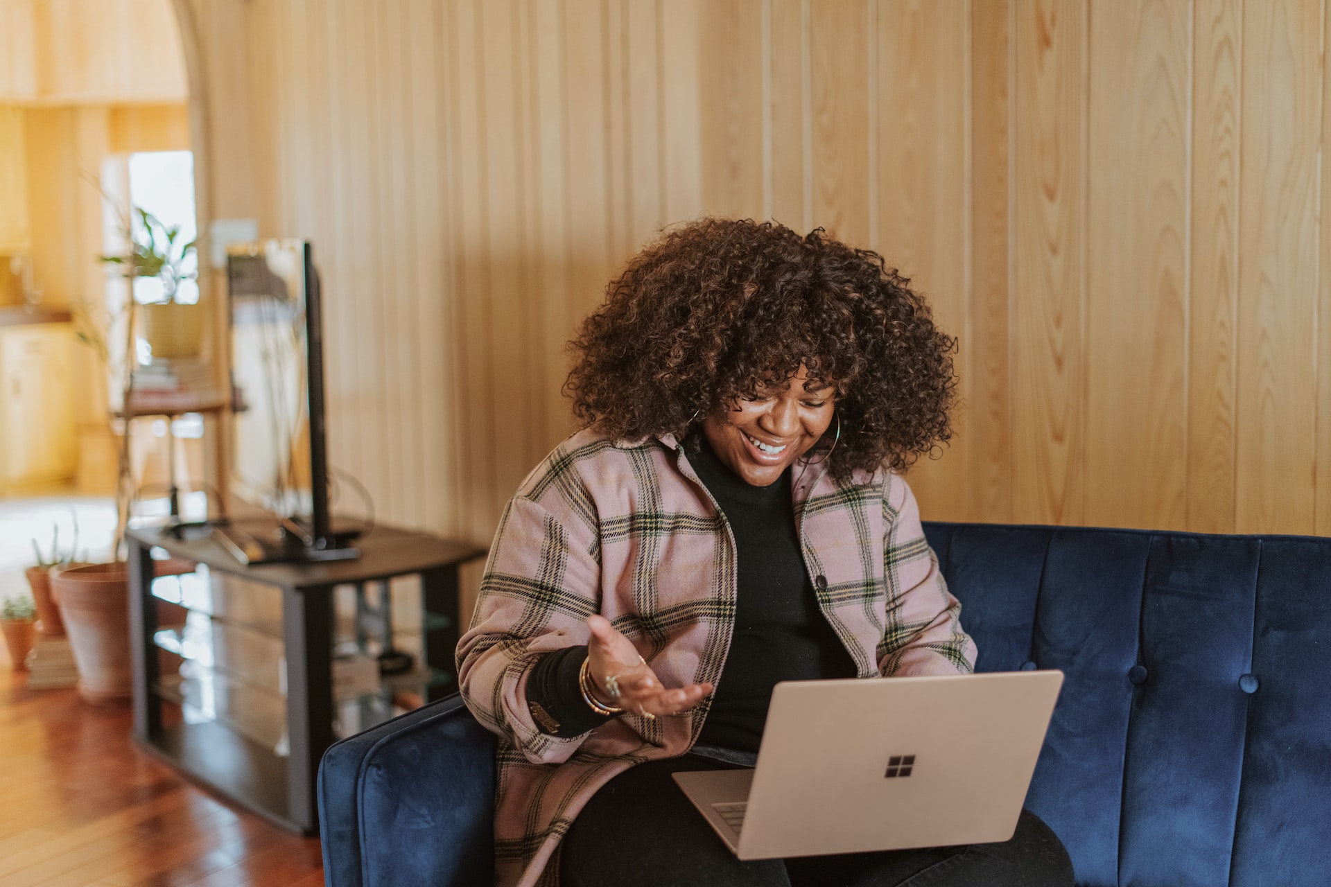 A black woman sitting on a couch and talking on a video call in front of a laptop