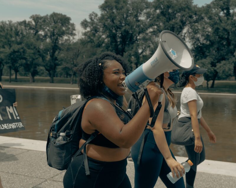 A black woman walking while speaking into a megaphone